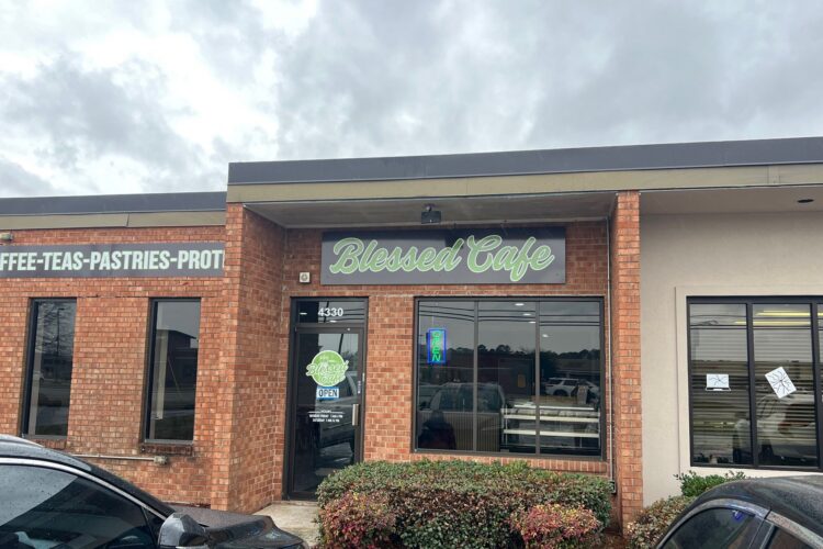 Exterior of Blessed Cafe in Lumberton, NC, a brick building with large windows under a cloudy sky.