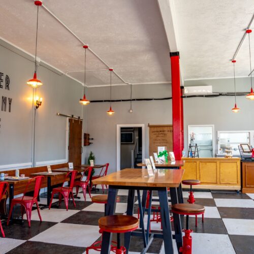 Ladder Company Cafe sitting area with bright red chairs and bar stools. Alongside sleek wooden tables atop a checkered floor.