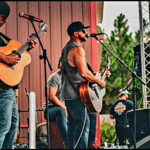 Musician Mark McKenney performing live while singing into a microphone and playing the guitar in Lumberton, NC.