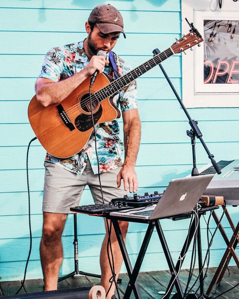Matt Letch holding a microphone and guitar in Lumberton, NC in front of a bright teal wall