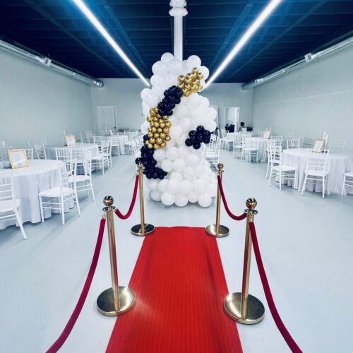Interior of The Kinship in Lumberton, NC showing white tables and chairs, a red carpet, and a balloon sculpture