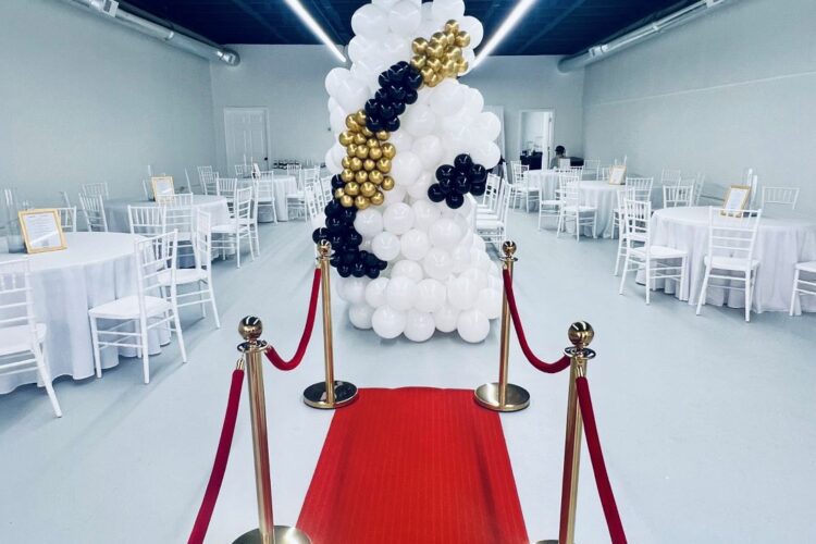 Interior of The Kinship in Lumberton, NC showing white tables and chairs, a red carpet, and a balloon sculpture