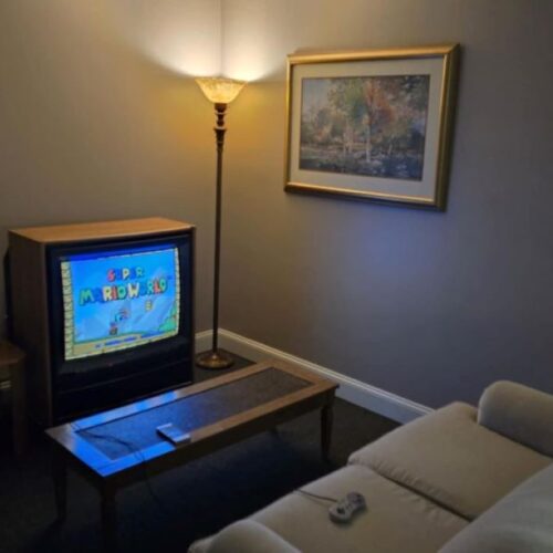 A vintage TV with Super Mario World on it in a living room with a couch, coffee table, and lamp