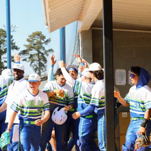 Baseball players in a dugout celebrate, cheering and raising their hands in excitement.