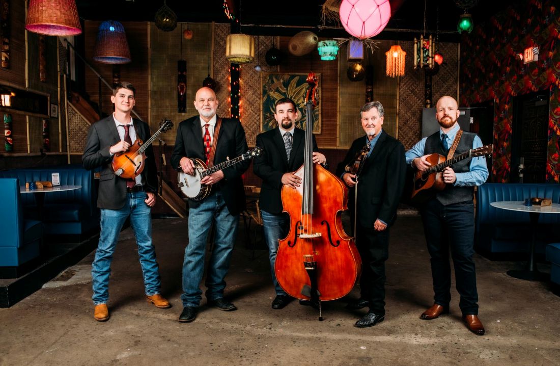 Five men dressed in western attire with each holding either a banjo, guitar, cello, or violin